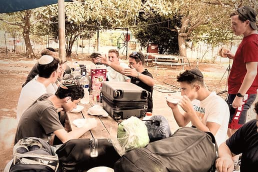 Torah Tech students eating together at long outdoor tables on a trip